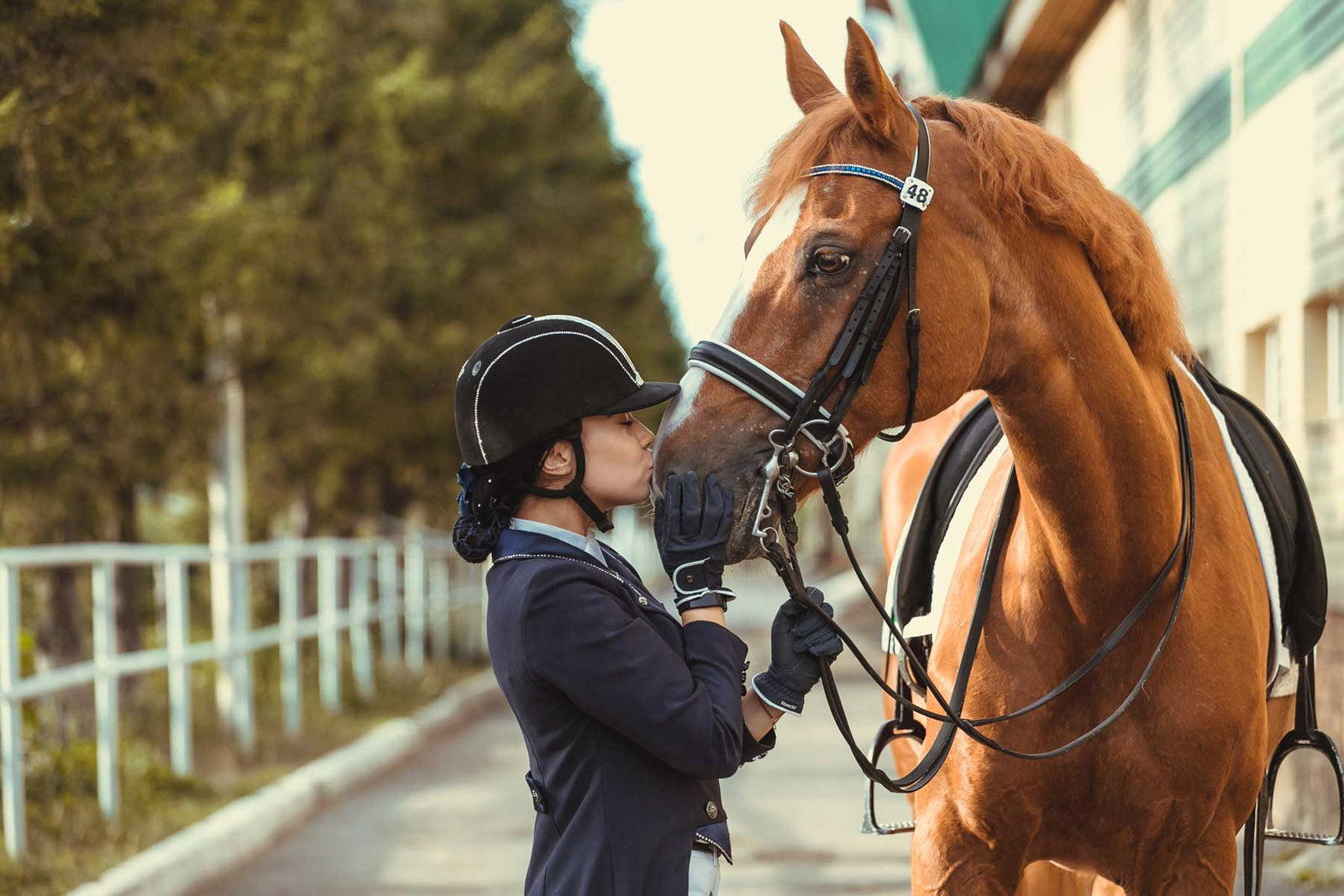 girl in front of barn kissing her horse